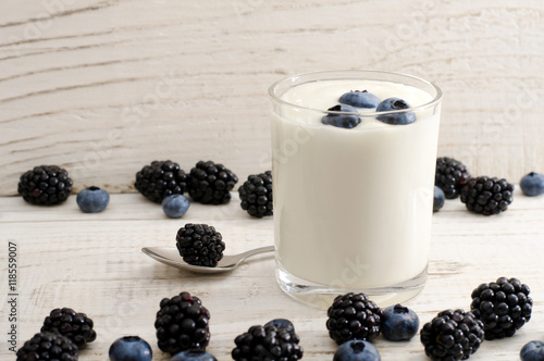 Glass of yogurt with blueberries, blackberries in a spoon