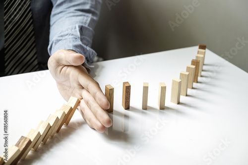 a male hand stopping the domino effect. retro style image executive and risk control concept
