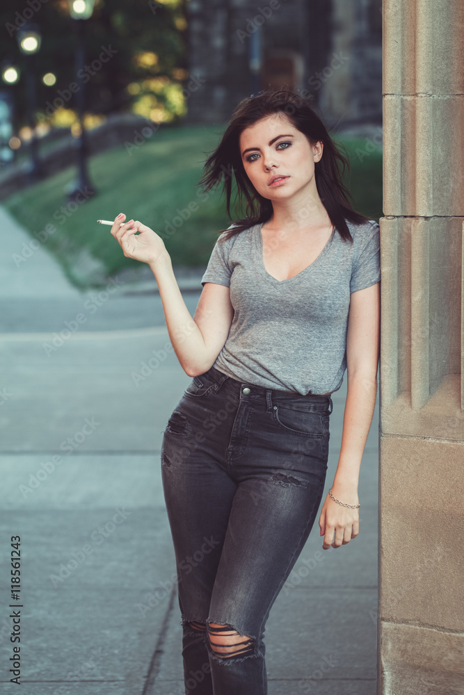 Portrait of white Caucasian beautiful young brunette woman teenager in jeans  and t-shirt outside in urban city on sunset smoking cigarette looking in  camera, toned with Instagram filters Stock Photo | Adobe