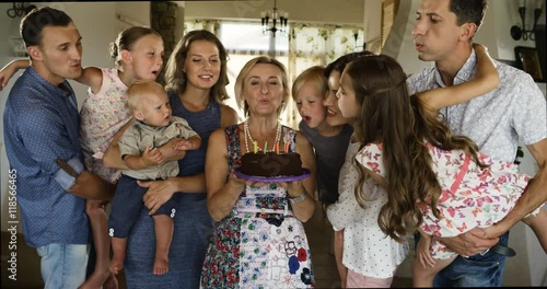 Multi generation family celebrating birthday at home, blowing out candles on birthday cake