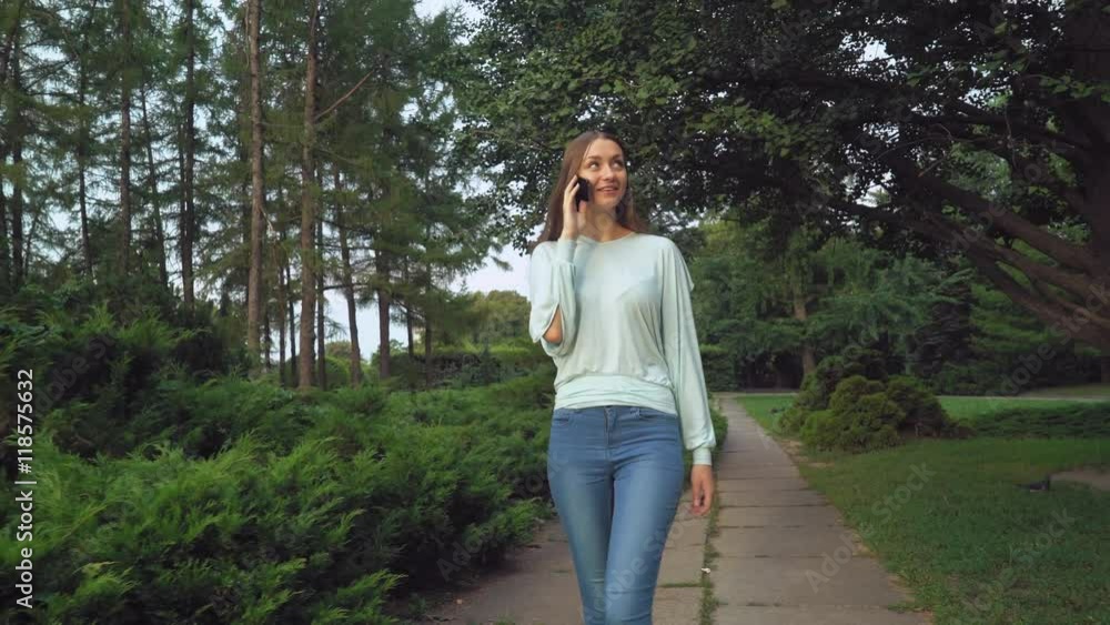 A young girl in a green blouse with long hair park talking and talking on the phone, smiles, surprised, enjoying the view. A young girl in a green blouse with long hair park talking and talking on the phone, smiles, surprised, enjoying the view.