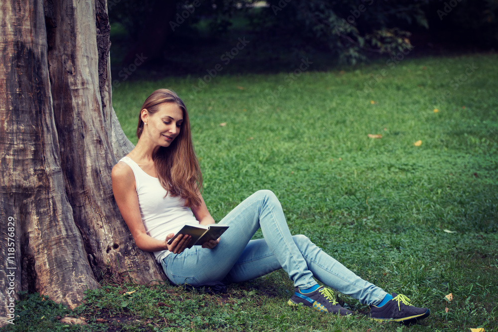 Young woman sitting on the grass and reading book outdoor. Young woman sitting on the grass and reading book outdoor.