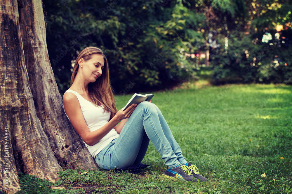 Young woman sitting on the grass and reading book outdoor. Vintage filtered image Young woman sitting on the grass and reading book outdoor. Vintage filtered image