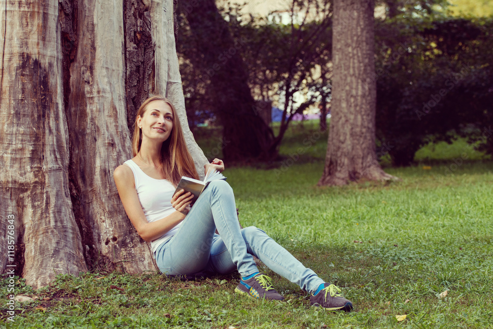 Young woman sitting on the grass and reading book outdoor. Vintage filtered image Young woman sitting on the grass and reading book outdoor. Vintage filtered image