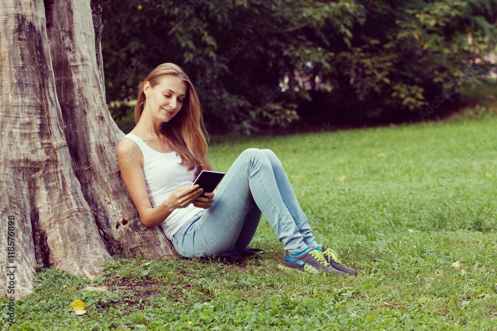 Young woman sitting on the grass and reading book outdoor. Vintage filtered image Young woman sitting on the grass and reading book outdoor. Vintage filtered image