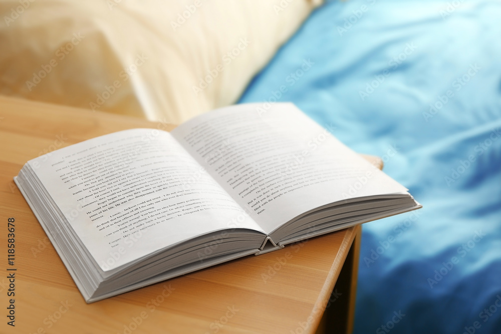 Fototapeta premium Opened book on wooden bedside table near crumpled bed