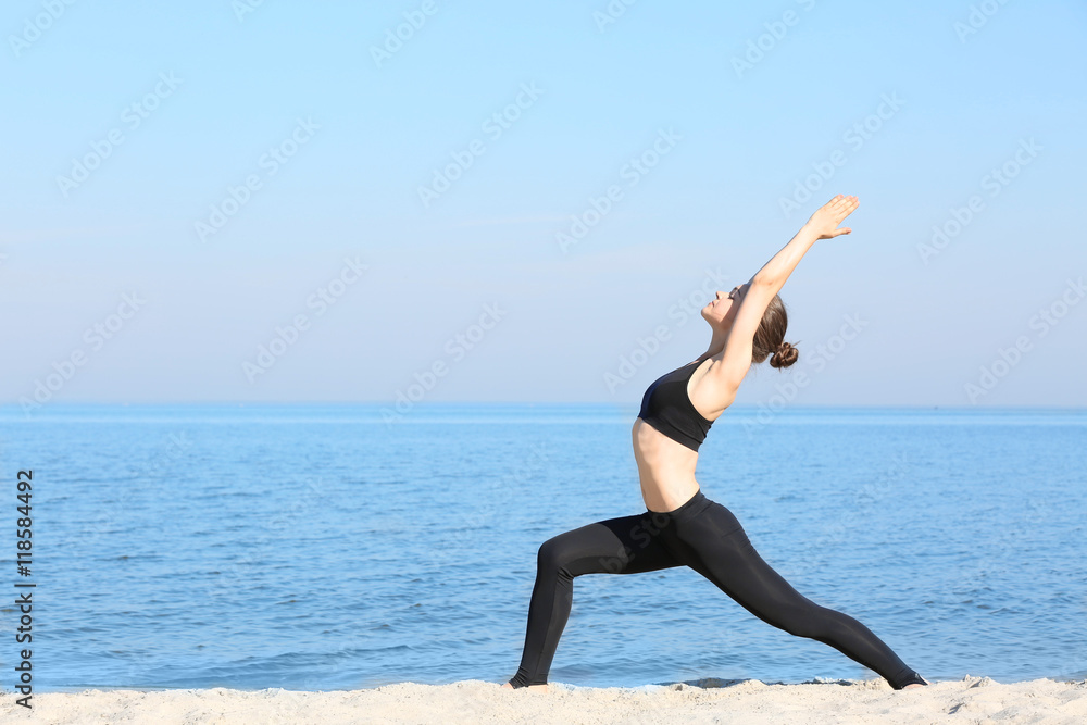 Fototapeta premium Attractive young woman doing yoga by the sea