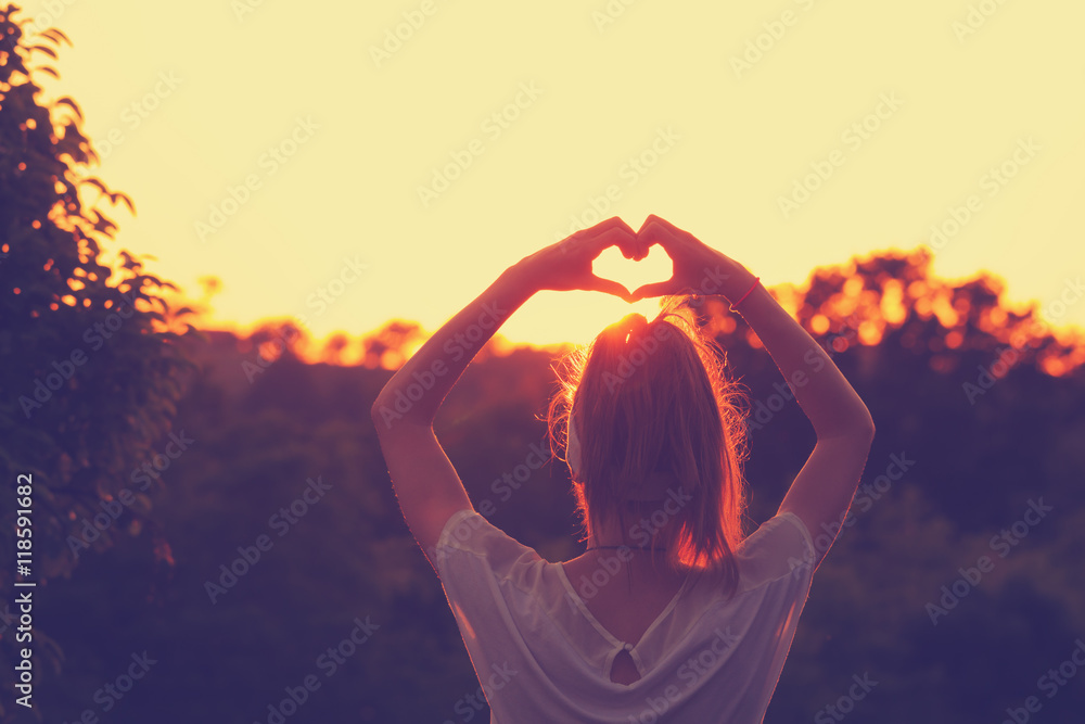 Girl making a heart-shape for the sunset. - obrazy, fototapety, plakaty 