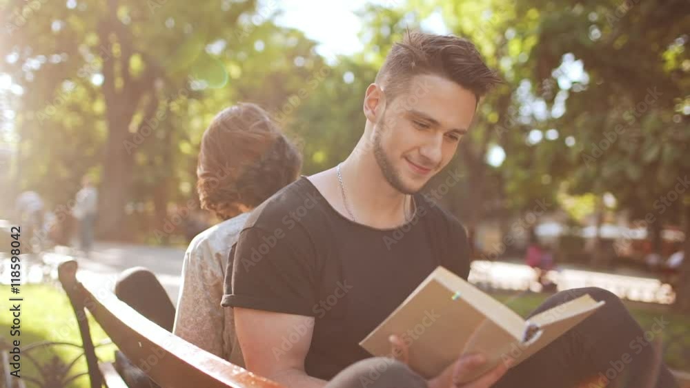 Young beautiful couple smiling, reading book, sitting in city park. Slow motion. Young beautiful couple smiling, reading book, sitting in city park. Slow motion.