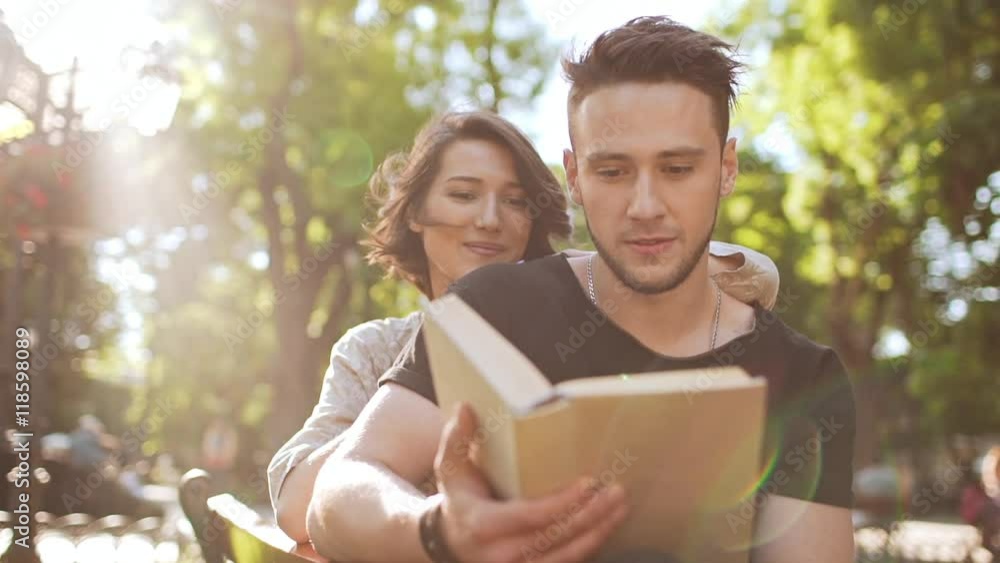 Young beautiful couple smiling, reading book, sitting in city park. Slow motion.