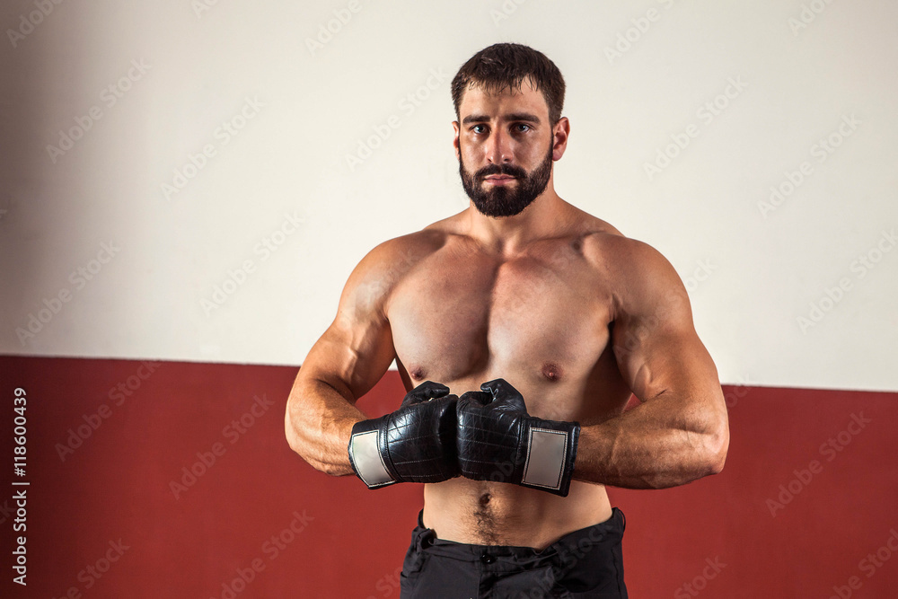 Muscular boxer in boxing gloves is looking at the camera.