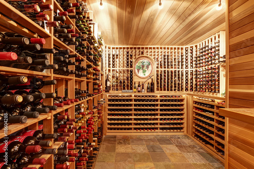 Foto Bright home wine cellar with wooden storage units with bottles.