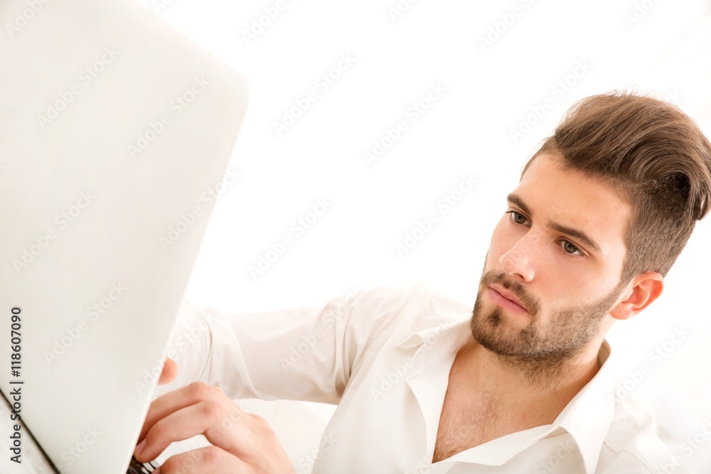 Attractive young man sitting at the table with a laptop computer.. Attractive young man sitting at the table with a laptop computer..