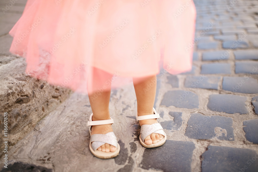 Tiny little feet of a girl in pink dress stand on the carriage w