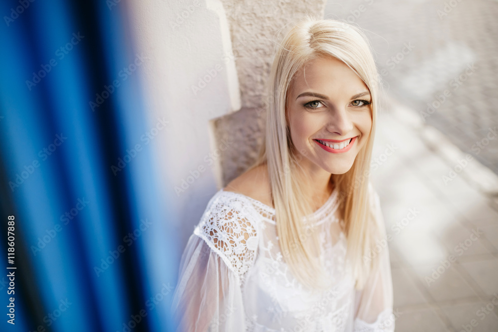 Look from behind blue curtain at smiling blonde sitting outside Look from behind blue curtain at smiling blonde sitting outside