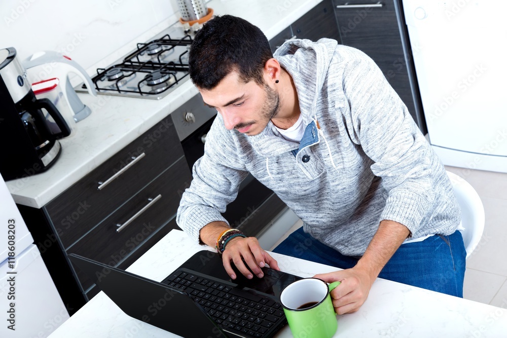 Portrait of a young man in the kitchen with a laptop.. Portrait of a young man in the kitchen with a laptop..