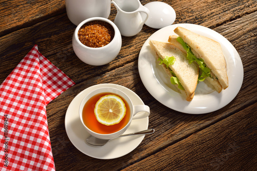 Cup of tea with lemon and sandwich on wooden background