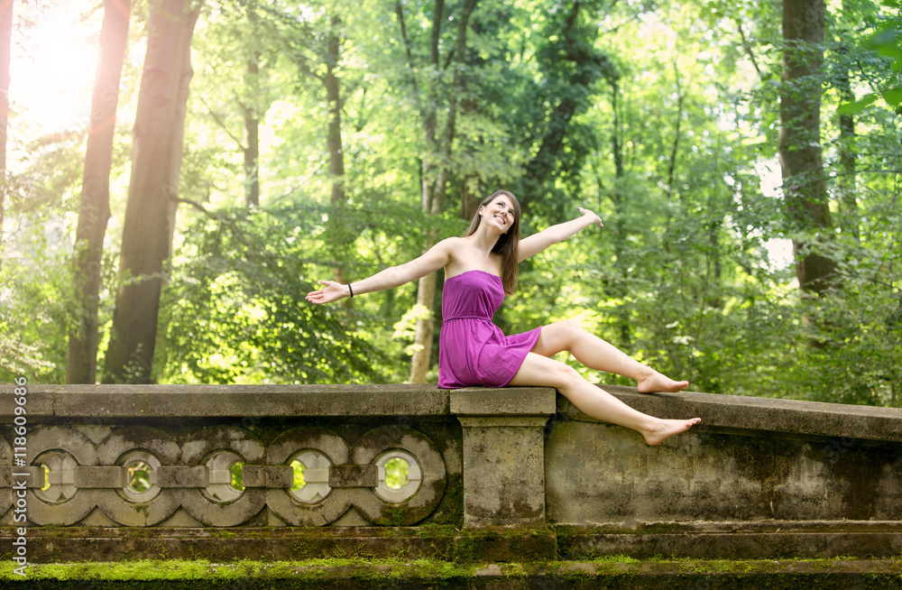 young woman sitting on bridge in park looking happy young woman sitting on bridge in park looking happy