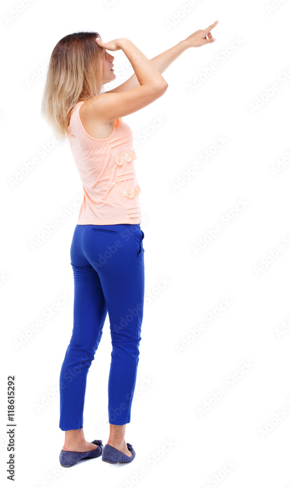 Back view of pointing woman. beautiful girl. Rear view people collection. backside view of person. Isolated over white background. Blonde in blue pants looks into the distance and points a finger. Back view of pointing woman. beautiful girl. Rear view people collection. backside view of person. Isolated over white background. Blonde in blue pants looks into the distance and points a finger.
