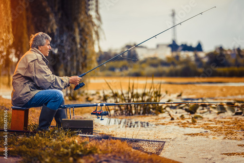 Senior man fishing on a freshwater lake sitting patiently  photo