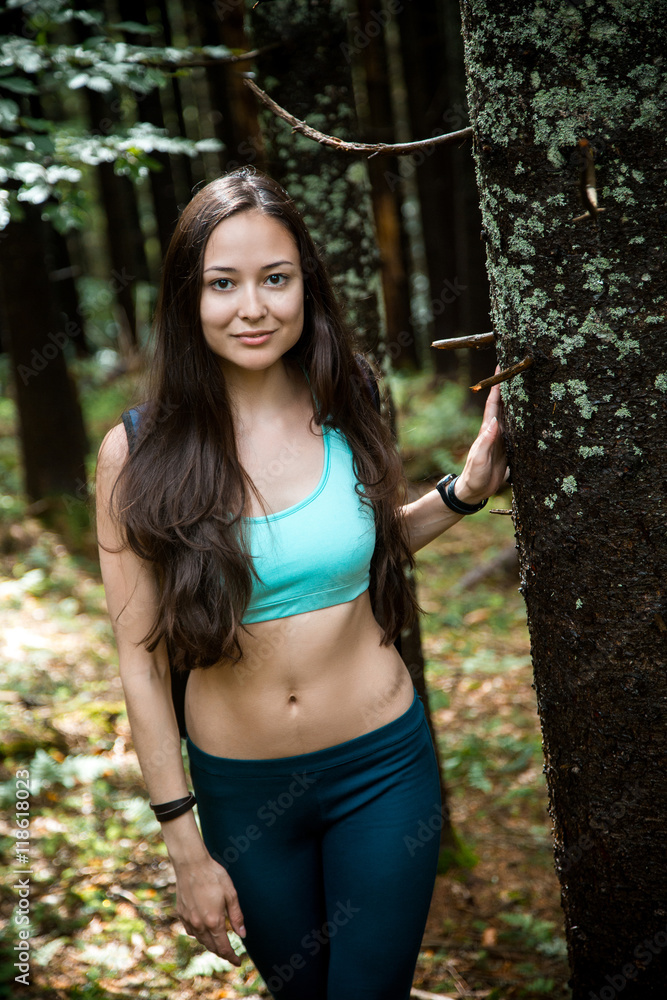 Young beautiful girl tourist with a Hiking backpack and a sports figure walking in the woods