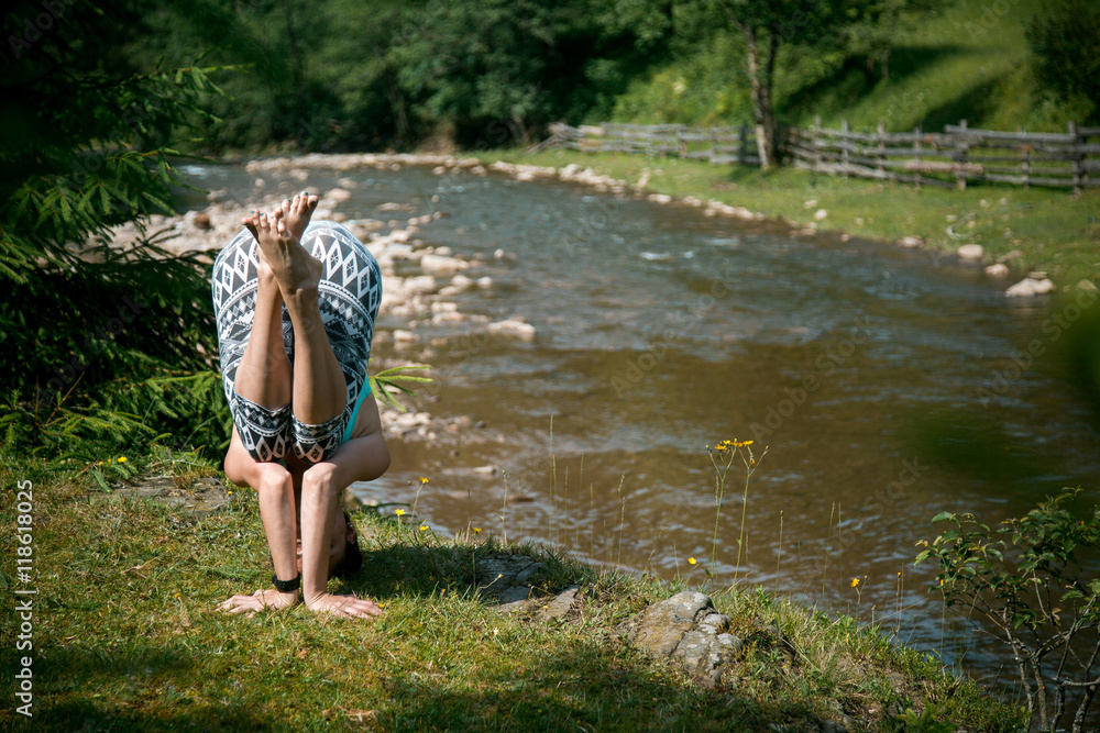 Young beautiful girl with nice body stands on the head during yoga on the shore of a mountain river.