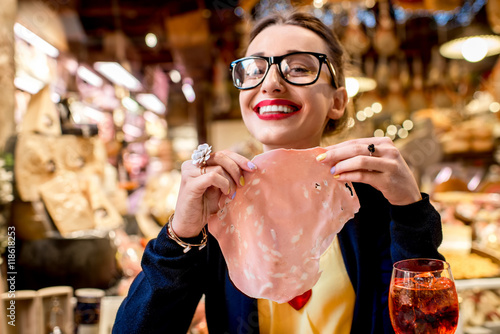 Young woman with big slice of mortadella sausage in front of food showcase in Bologna city. Mortadella was invented in Bologna city
