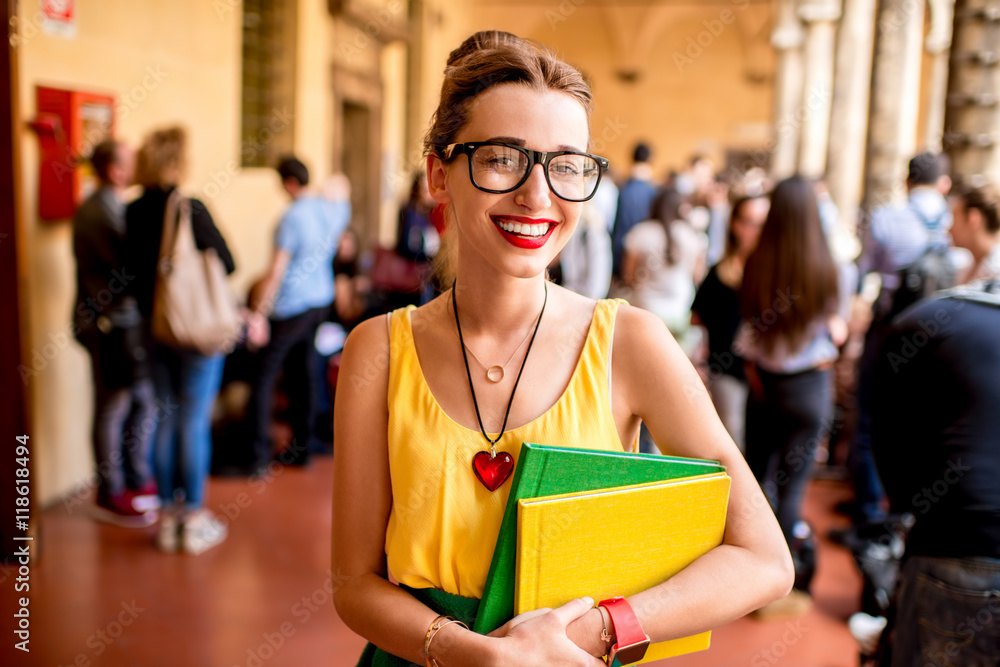 Portrait of a young female student dressed casually with colorful books during the break in crowded corridor at the old university Portrait of a young female student dressed casually with colorful books during the break in crowded corridor at the old university