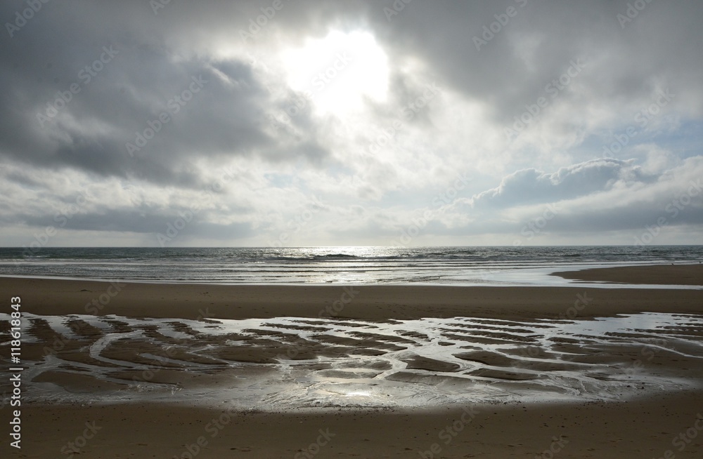 Abendstimmung mit dunklen Wolken und durch Wasser entstandenes Muster im Sand