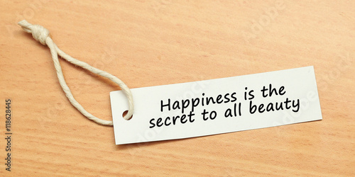 White tag on wooden background with word quotes of Happiness is the secret to all beauty photo