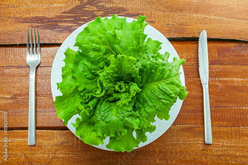Plate of fresh green lettuce with silverware on a table. Abstract concept of healthy vegetarian food. Top view.