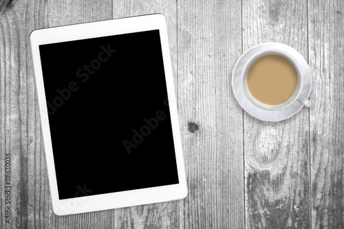 White tablet with a coffee cup on old wooden table. Blank screen with space for copy. Concept the coffee break with the use of the tablet.