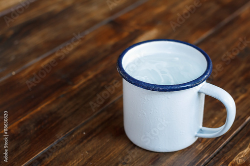 Mug of cool water with ice on wood table. Soft focus.