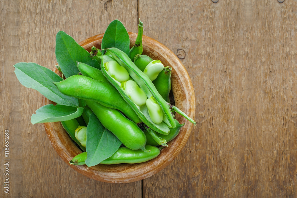 Fresh green broad beans in a bowl. Fresh raw vegetables on a wooden table. Ingredients healthy vegetarian food. Fresh green broad beans in a bowl. Fresh raw vegetables on a wooden table. Ingredients healthy vegetarian food.