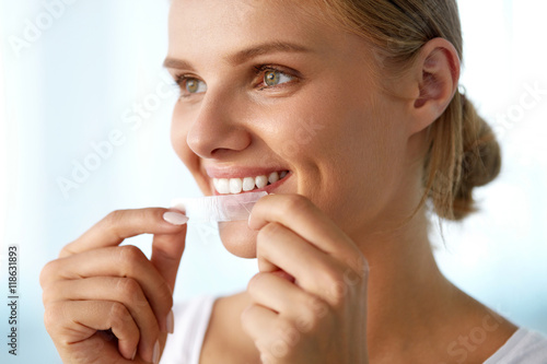 Fototapeta Naklejka Na Ścianę i Meble -  Woman With Healthy White Teeth Using Teeth Whitening Strip. High Resolution Image