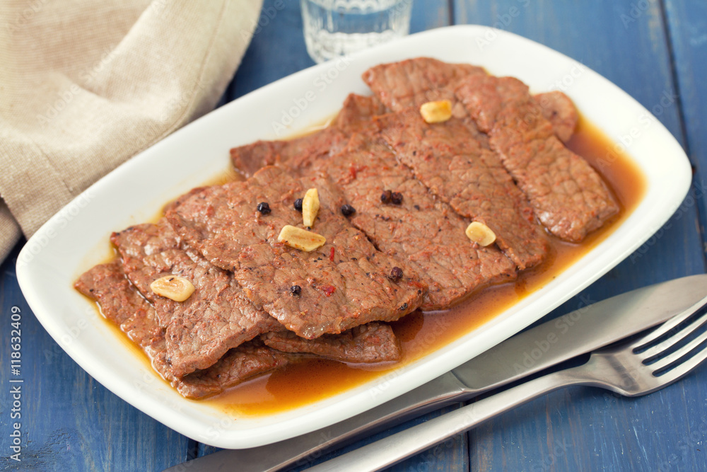 fried meat with sauce on white plate on blue wooden background.