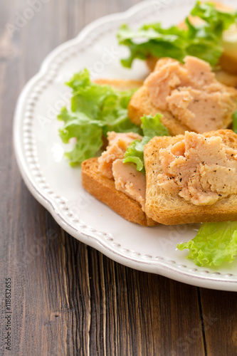 fish pate on toatst on white plate on brown wooden background © Natalia Mylova