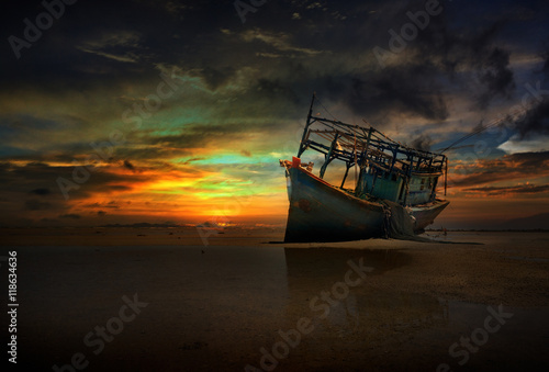 old abandoned boat on the shore under twilight which illuminates him hull and a dramatic cloudy sky
