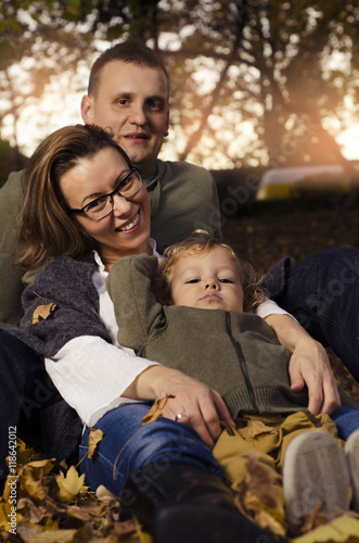 Happy family sitting in autumn leaves, mother, father and little son.