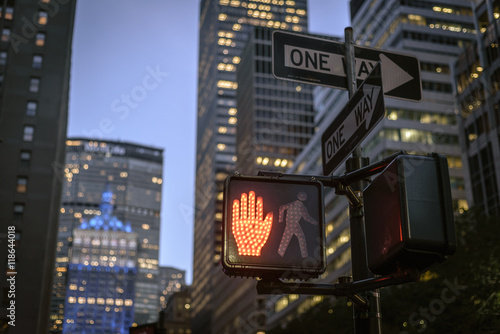 New York City red stop crosswalk sign on busy one way street with sunset skyline in the background.