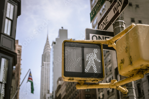 Yellow New York City crosswalk sign on busy one way street with skyline in the background.