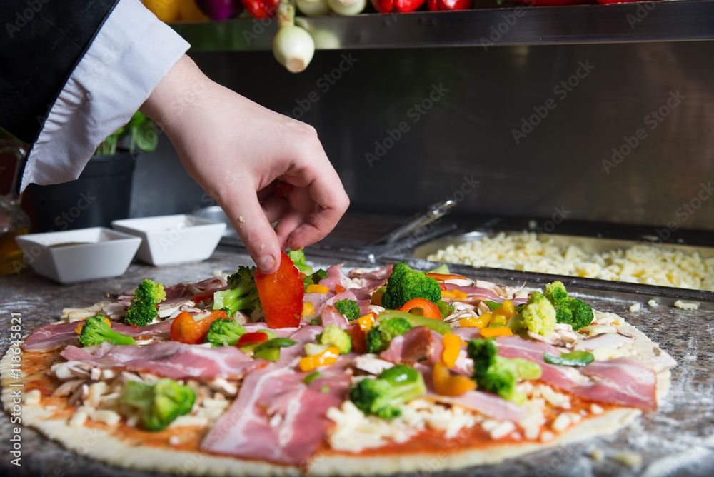 Preparating traditional pizza in profesional pizzeria. Chef is covered pastry by tomato sauce, mozarella cheese, mushrooms, bacon and fresh vegetables like pepper and broccoli. Preparating traditional pizza in profesional pizzeria. Chef is covered pastry by tomato sauce, mozarella cheese, mushrooms, bacon and fresh vegetables like pepper and broccoli.