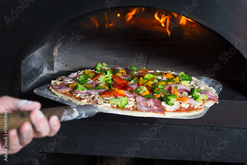 Chef puts pizza to the wood-fired oven which is very hot. He is transporting pastry at special showel. photo