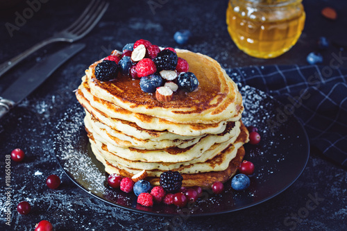 Delicious pancakes with fresh berries and honey on dark slate background