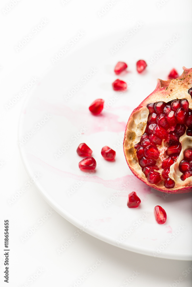 half pomegranate fruit with seeds spread in a white plate, closeup, vertical half pomegranate fruit with seeds spread in a white plate, closeup, vertical