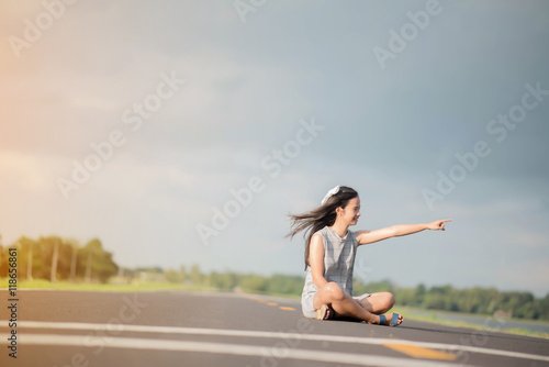 young woman sitting hitchhiking on a road with a suitcase