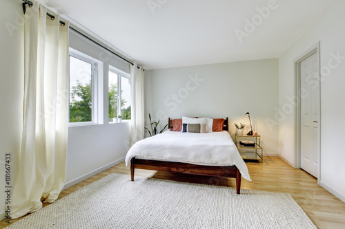 Bedroom interior in light tones with wooden bed and hardwood floor.