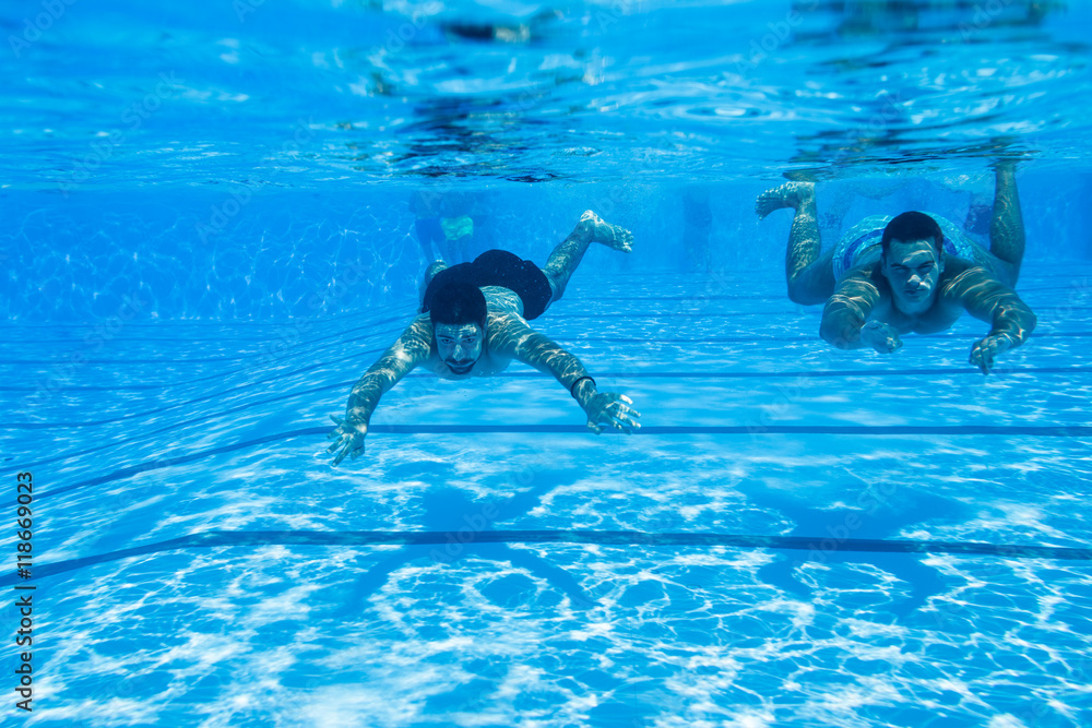 Underwater fun. Two young handsome men swimming underwater and diving in the swimming poll. Sport and leisure.
