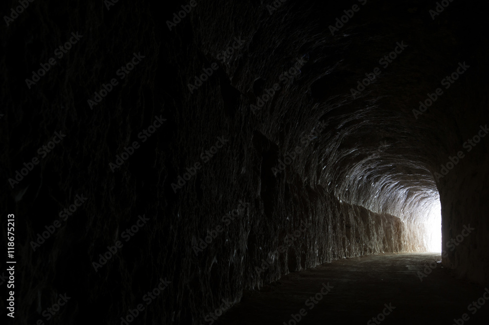 Dark road in a natural rocky tunnel and the light of the exit