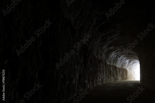 Fototapeta Dark road in a natural rocky tunnel and the light of the exit
